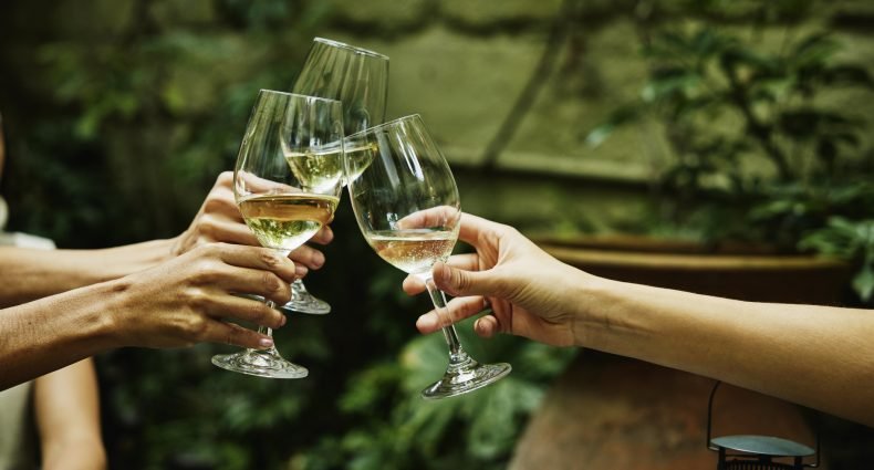 Mãos segurando taças de vinho pela haste durante um brinde, mostrando como segurar a taça de vinho corretamente para melhorar a experiência de degustação.