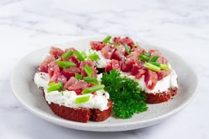 Bruschettas com peixe cru em cubos (tipo tartare), creme branco e cebolinha em prato, ilustrando iniciativas do Pão de Açúcar com pescados sustentáveis e rastreabilidade.